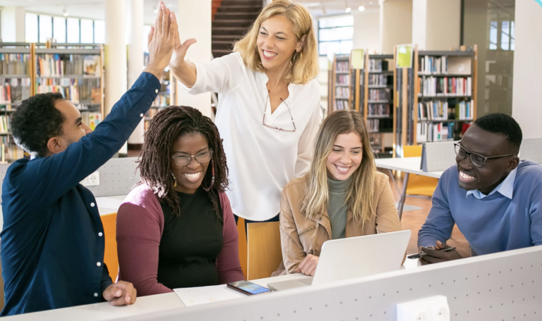 Team working on Computers and 2 members clapping in a high five.